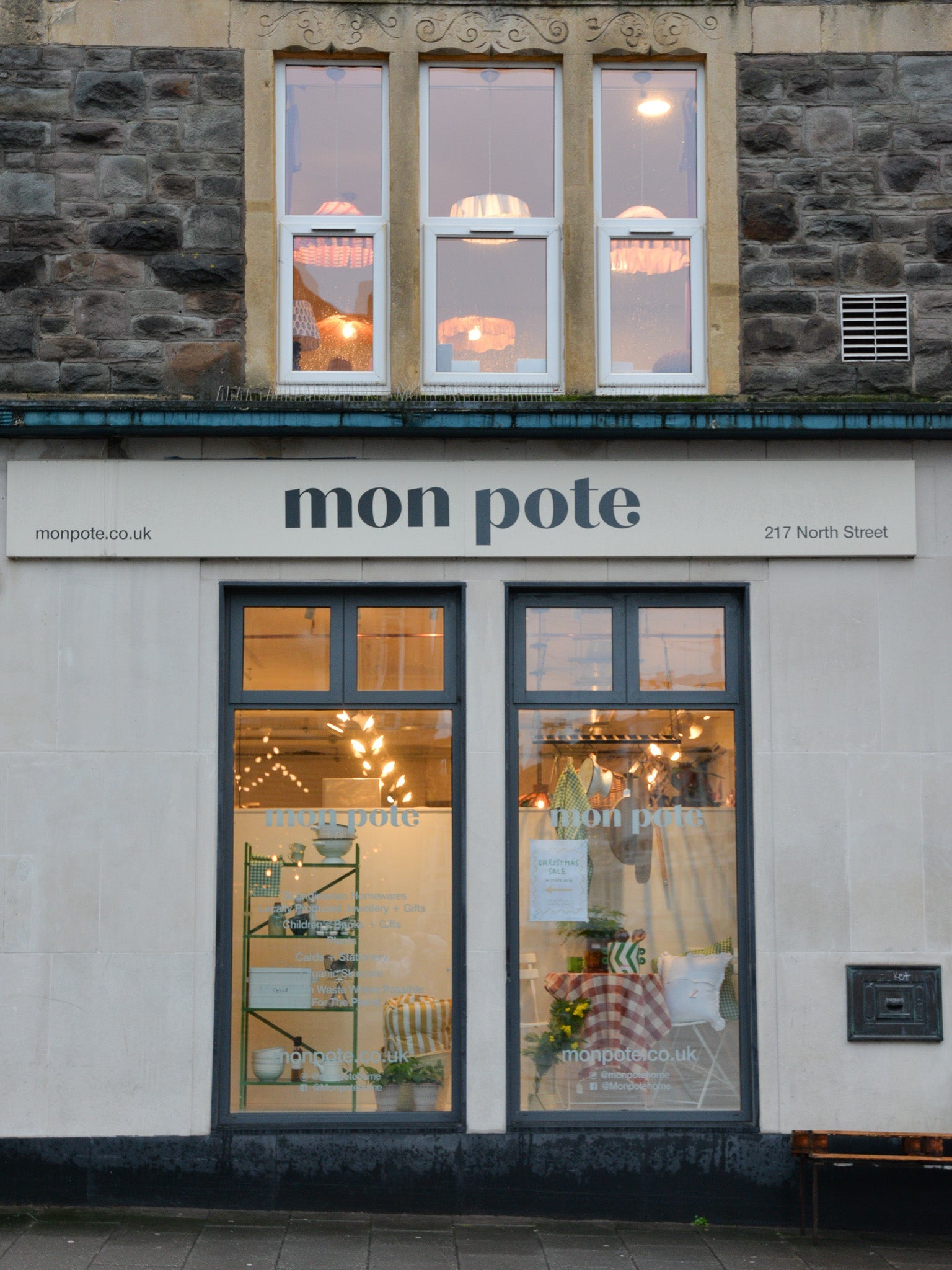 Exterior of Mon Pote at dusk with warm glowy lights and our spring like window display