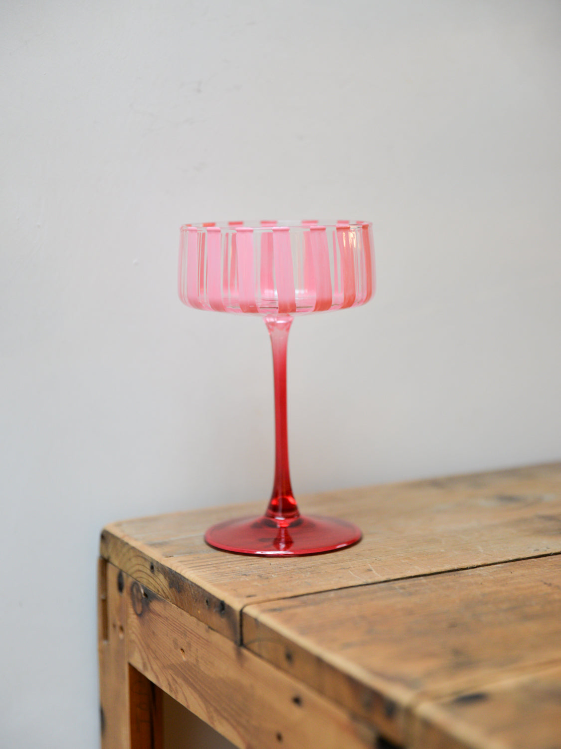 Pink glass cocktail coupe on a wooden surface with a plain background